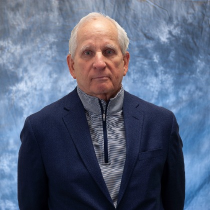 A person with dark hair appears in front of a cloudy blue backdrop.